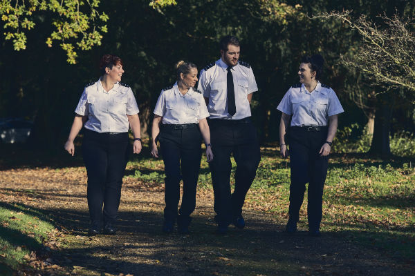 4 prison officers, 1 male, 3 female, walk through a wooded area. They are chatting and smiling.