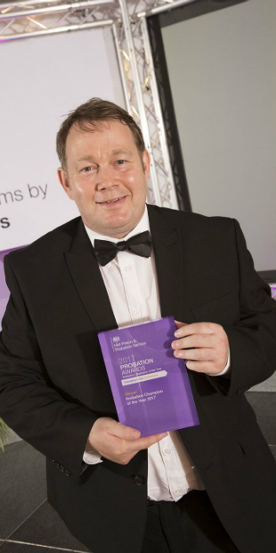 Gareth is dressed in a tuxedo and holds a purple glass rectangular award for 2017 probation champion