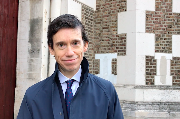 Prisons Minister Rory Stewart smiling, wearing a shirt tie and coat, standing in front of a brick wall outside HMP Wormwood Scrubs